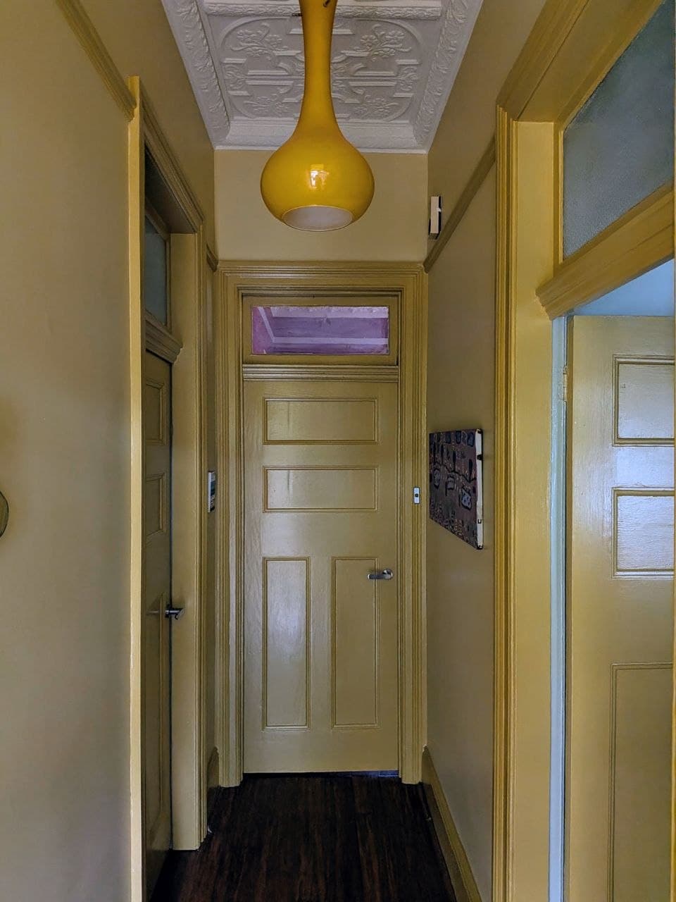 The same hallway after repainting — warm mustard walls, crisp white pressed-tin ceiling and a rich timber floor